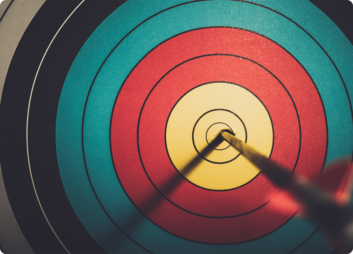 Renkli bir hedef tahtasının tam merkezine (on ikiden) saplanmış bir ok.